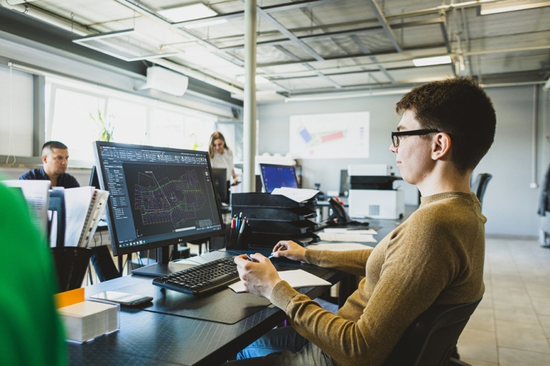 Инженер ведёт в AutoCAD plan‑схему трубопроводной сети; на стене - схема производственной площадки